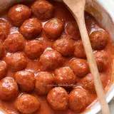 Polpette al sugo succulente in una ciotola bianca, pronte per essere gustate. Un cucchiaio di legno le accompagna.