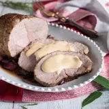 Arrosto di vitello morbido con sughetto benedetta, servito su un piatto bianco con cipolle rosse e rosmarino.