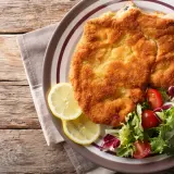 Una dorata cotoletta alla milanese, croccante e succulenta, servita con spicchi di limone e un'insalata fresca.