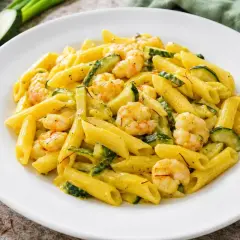 Piatto di pasta penne con zucchine e gamberetti, condita con una salsa cremosa e fili di zafferano.