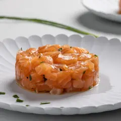 Tartare di salmone fresco, finemente tagliato e condito, servito su un piatto bianco con erba cipollina.