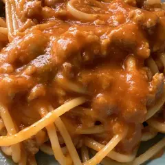 Un piatto di spaghetti al ragù, con un sugo ricco e saporito, dove spiccano i pomodorini.