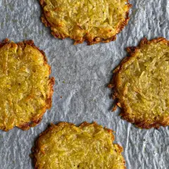 Quattro rosti di patate dorati e croccanti su carta da forno.