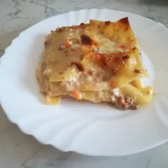 Porzione di lasagna classica, con strati di pasta, ragù e besciamella, servita su un piatto bianco.