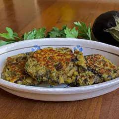 Tre hamburger di melanzane dorati e appetitosi in un piatto decorato, con un'altra melanzana e prezzemolo sullo sfondo.