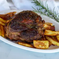 Stinco di maiale arrosto, dorato e succulento, servito con patate croccanti e rosmarino fresco.