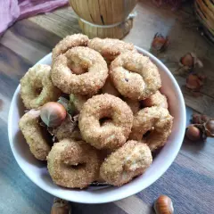 Ciambelline al vino cosparse di zucchero, con nocciole e un drappo rosa su un tavolo di legno.
