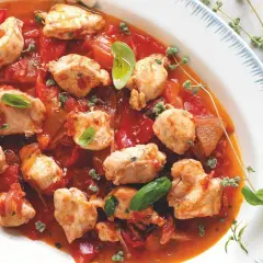 Piatto di coniglio alla cacciatora ricetta della nonna, con pezzi di carne tenera in salsa di pomodoro e peperoni, guarnito con basilico fresco e timo.