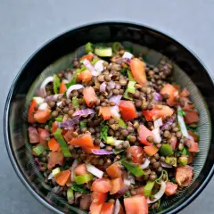 Una ciotola di insalata di lenticchie colorata con pomodori, cipolla rossa e erbe fresche.