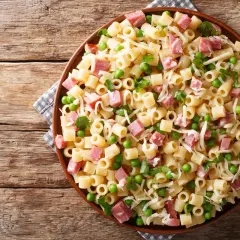 Un piatto di pasta con prosciutto cotto, piselli e formaggio grattugiato su un tavolo di legno rustico.