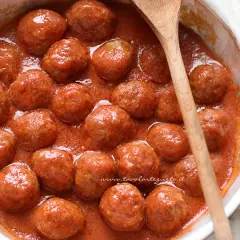 Polpette al sugo succulente in una ciotola bianca, pronte per essere gustate. Un cucchiaio di legno le accompagna.