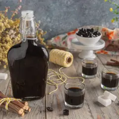 Bottiglia di liquore alla liquirizia scuro, bicchierini, bastoncini di liquirizia, zollette di zucchero e caramelle nere su un tavolo di legno.