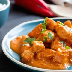 Bocconcini di pollo in salsa cremosa, guarniti con prezzemolo fresco, accompagnati da riso bianco e spicchio di lime.