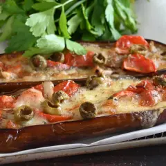Melanzane alla pizzaiola, gustose e filanti, con pomodoro, olive e formaggio fuso, guarnite con prezzemolo fresco.
