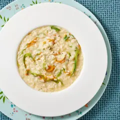 Un piatto di risotto ai fiori di zucca cremoso, con petali arancioni e fili verdi che si intrecciano nel riso bianco.