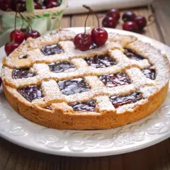 Deliziosa crostata senza burro con marmellata di ciliegie, cosparsa di zucchero a velo e decorata con ciliegie fresche.