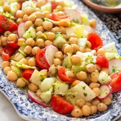 Un'insalata di ceci fresca e colorata con pomodorini, cetrioli e ravanelli, condita con erbe aromatiche.