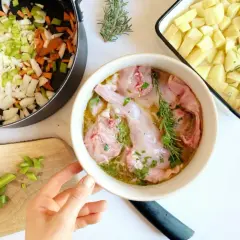 Preparazione per un coniglio alla cacciatora in bianco: pezzi di coniglio crudo in una ciotola, verdure tritate in padella e patate a cubetti in una teglia.
