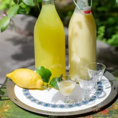 Due bottiglie di limoncello, una chiara e una cremosa, con limone fresco e bicchierini pronti per un assaggio.