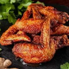 Alette di pollo al forno dorate e succulente, servite su una pietra scura con coriandolo, zenzero e aglio.