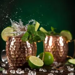 Moscow Mule ricetta: due tazze di rame con schizzi d'acqua, lime, menta e cetriolo. Fresco e dissetante.