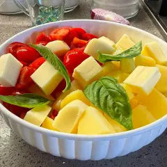 Insalata di pomodori freschi, cubetti di formaggio e foglie di basilico in una ciotola bianca.