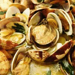 Un invitante sautè di vongole, con gusci aperti che rivelano la loro polpa succulenta, immersi in un brodo profumato.