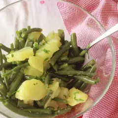 Insalata di fagiolini e patate, condita con erbe fresche, servita in una ciotola di vetro su un tovagliolo a quadretti rossi.