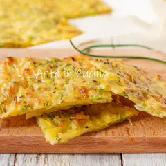 Schiacciata di zucchine dorata e croccante, condita con erbe aromatiche, servita su un tagliere di legno.