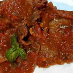 Fette di carne alla pizzaiola siciliana, ricoperte da un sugo rosso saporito e guarnite con basilico fresco.