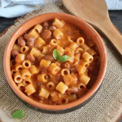 Un piatto fumante di pasta e fagioli in scatola, guarnito con menta fresca, servito in una ciotola di terracotta su una tovaglietta di juta.