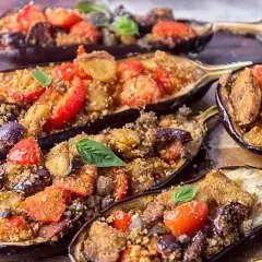 Melanzane a scarpone ripiene di pomodorini, olive e pangrattato, guarnite con basilico fresco. Un piatto saporito e invitante.