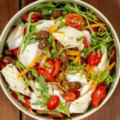 Insalata di calamari fresca con pomodorini, olive, rucola e carote julienne, un piatto estivo colorato e saporito.