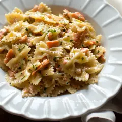 Farfalle cremose con salmone affumicato, un piatto delizioso e invitante, guarnito con prezzemolo fresco e pepe nero.