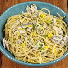 Spaghetti con acciughe, prezzemolo tritato e scorza di limone grattugiata in una ciotola blu su un tavolo di legno.