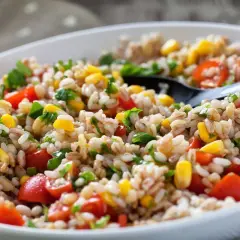 Insalata di farro colorata con pomodorini, mais e prezzemolo fresco, servita in una ciotola bianca.