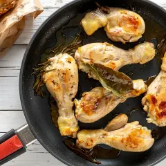 Fusi di pollo in padella, dorati e succulenti, con rosmarino e alloro. Accanto, panini integrali appena sfornati.