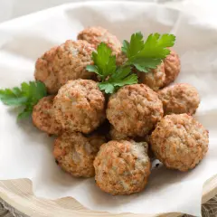 Un mucchio di polpette di pollo dorate e profumate, guarnite con prezzemolo fresco, servite su carta da forno in un piatto di legno.