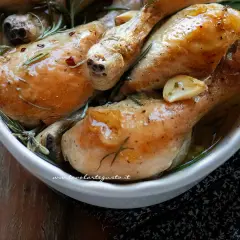 Cosce di pollo al forno succulente, dorate e profumate al rosmarino e aglio, servite in una ciotola bianca.