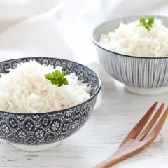 Due ciotole di riso in bianco, guarnite con prezzemolo, su un tavolo di legno. Un cucchiaio di legno è posizionato accanto.