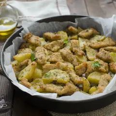 Straccetti di pollo al forno con patate, dorati e croccanti, guarniti con prezzemolo fresco.