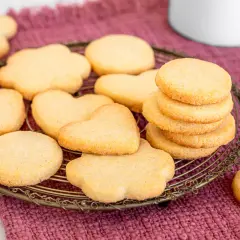 Deliziosi dolci da fare in casa: biscotti a forma di cuore e fiori su una gratella, con una pila di biscotti rotondi e un pezzo rotto in primo piano.