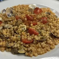 Un piatto invitante di fregola con vongole, pomodorini e prezzemolo, pronto per essere gustato.