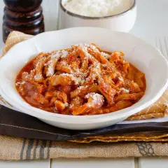Piatto fumante di trippa alla parmigiana, cosparsa di formaggio grattugiato, su un tavolo di legno.