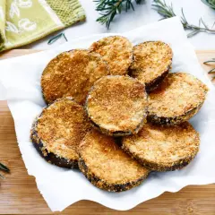 Cotolette di melanzane dorate e croccanti, servite su carta bianca con rametti di rosmarino.
