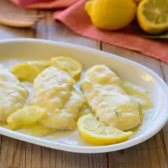 Scaloppine al limone cremose, succulente e profumate, guarnite con spicchi di limone fresco su un piatto bianco.