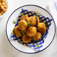 Piatto di polpette di ceci dorate e croccanti, guarnite con prezzemolo fresco. Accanto, ciotole con ceci e farina di ceci.