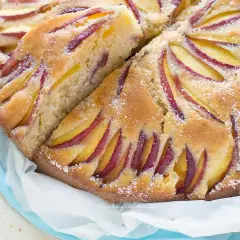 Una deliziosa torta di pesche, con fette di frutta disposte a raggiera sulla superficie dorata e cosparsa di zucchero.