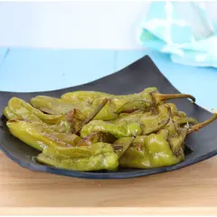 Friggitelli al forno, verdi e lucidi, serviti su un piatto nero. Un contorno saporito e facile da preparare.