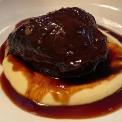 Guancia di manzo brasata, tenerissima e succulenta, adagiata su un letto di purè cremoso, il tutto avvolto da una ricca salsa scura.